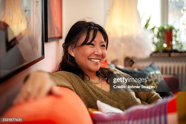smiling mature woman sitting on sofa at home - johner images stock pictures, royalty-free photos & images