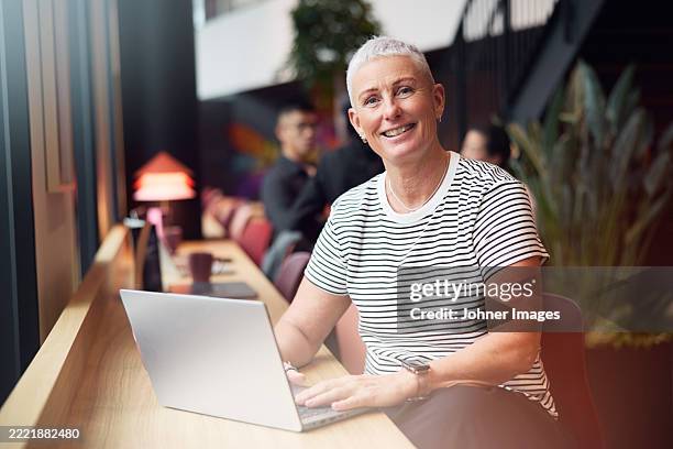 portrait of smiling short haired female entrepreneur sitting with laptop at work place - scandinavie photos et images de collection