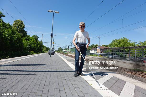 blind man walking on platform of small train station - blind persons cane stock pictures, royalty-free photos & images