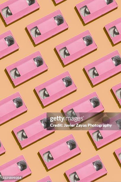 pink vhs cassettes arranged in a seamless pattern on an orange background - television set 1990s stock pictures, royalty-free photos & images