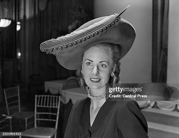 Model wears a hat with a dark brown top and a red underside, decorated with an Argus pheasant feather, on show at the Associated Millinery Designers...