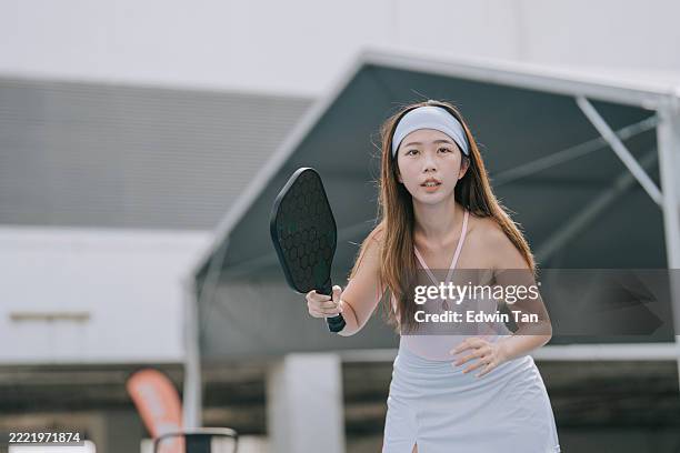 young asian woman focused while playing outdoor pickleball - paddle ball stock pictures, royalty-free photos & images