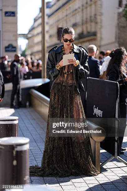 Guest wears a black leather jacket with structured shoulders over a sheer, flowing maxi dress featuring an intricate paisley pattern in shades of...