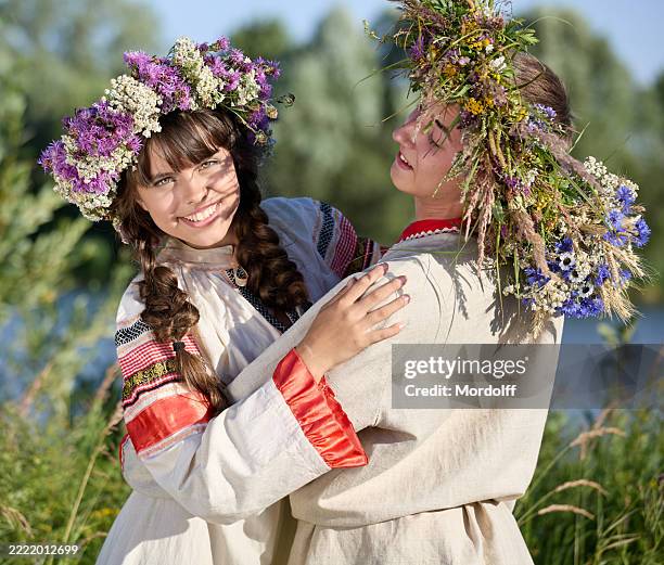 beautiful young couple in traditional slavic clothing and flower crowns hugging at a sunny day near a river at midsummer holiday - russian ethnicity stock pictures, royalty-free photos & images
