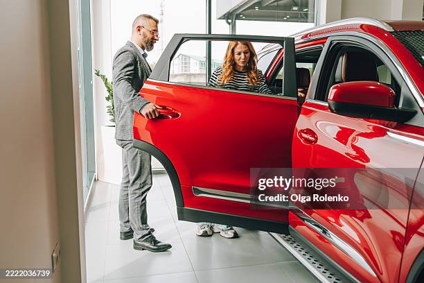 car salesman showing a new red car to a customer in a dealership - suv stockfoto's en -beelden
