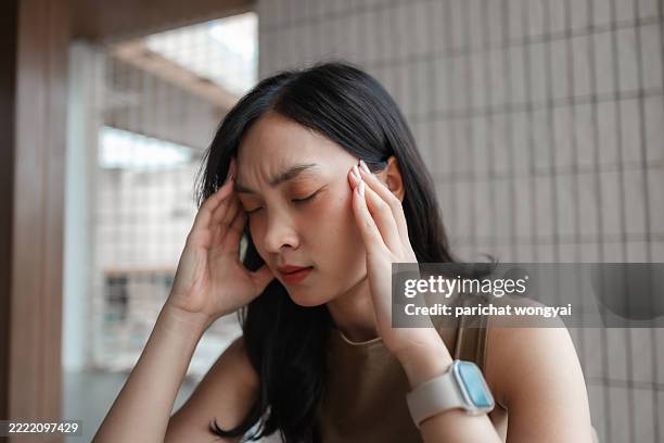 young asian woman suffering from a strong headache, touching her temples with her hands and closing her eyes - paranasal sinus stock pictures, royalty-free photos & images