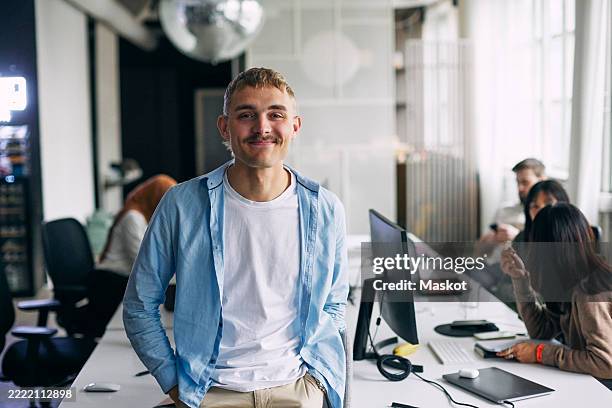portrait of smiling male entrepreneur leaning on desk at office - 20 29 år bildbanksfoton och bilder