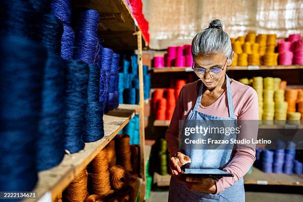 mature woman using digital tablet taking inventory at textile industry - textile industry stock pictures, royalty-free photos & images