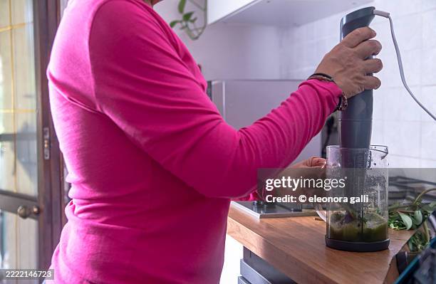 woman preparing green smoothie with hand blender in modern kitchen - batidor fotografías e imágenes de stock