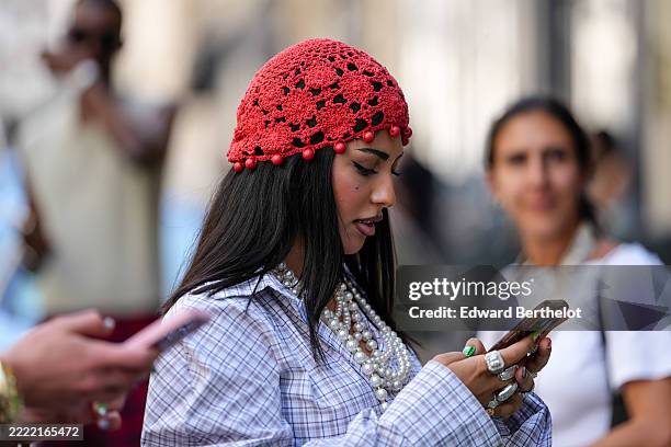 Guest wears a red crocheted headpiece adorned with small red beads along the edge. Hair is styled straight and long. Makeup includes defined eyeliner...