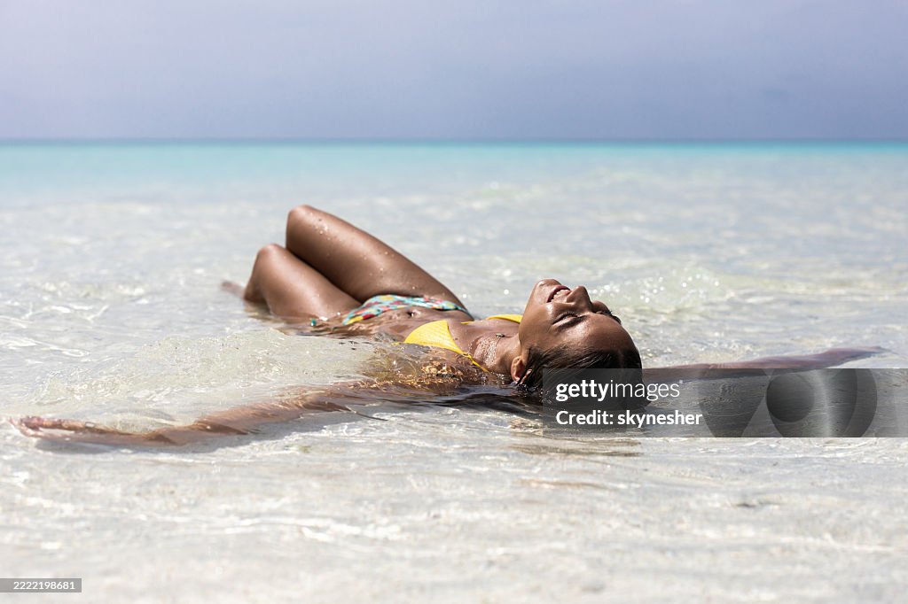 Happy woman enjoying while sunbathing in shallow water on the beach.