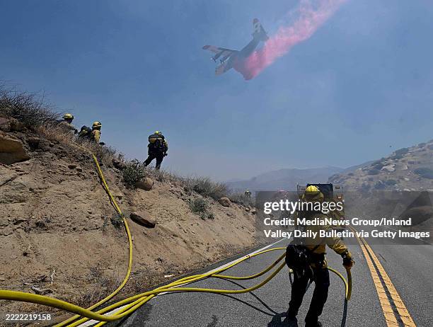 Banning, CA Firefighters pull hose lines along Highway 243, also known as the Esperanza Firefighters Memorial Highway, as a plane drops fire...