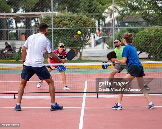 two double mixed gender pickleball players are playing on hardcourt ball is on air horizontal pickleball still - country club stockfoto's en -beelden