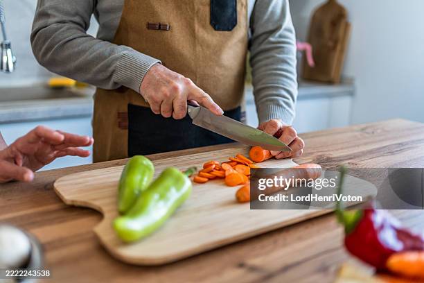 mature man cutting carrots and peppers in the kitchen - kitchen knife stock pictures, royalty-free photos & images