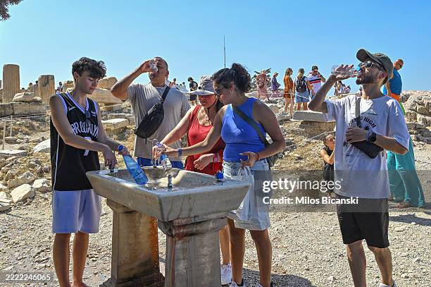Tourists refresh with water in front of the five century BC Parthenon temple at the Acropolis hill during a heat wave on June 25, 2025 in Athens,...