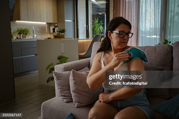 mature woman applying gel pack on her painful shoulder, ligament, muscle or bone problems. joint inflammation - inflamação imagens e fotografias de stock