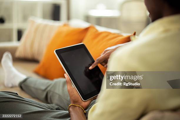 young man relaxing on sofa using digital tablet at home - on computer blank screen stock pictures, royalty-free photos & images