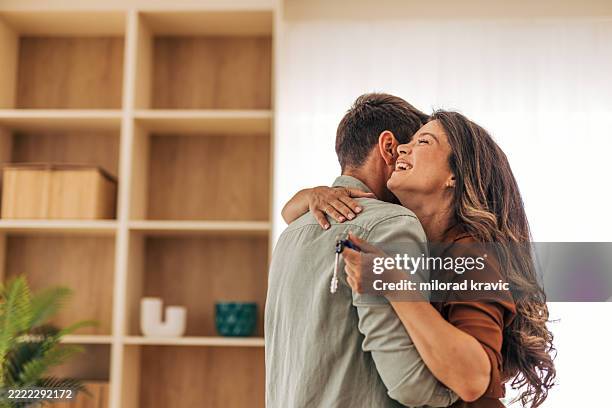 happy couple embracing and holding new house keys - moving house stock pictures, royalty-free photos & images