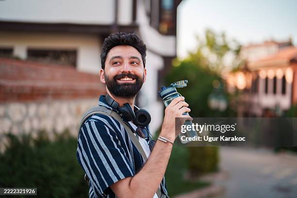 refreshing break: man drinking water from reusable bottle while walking - water bottle stock pictures, royalty-free photos & images