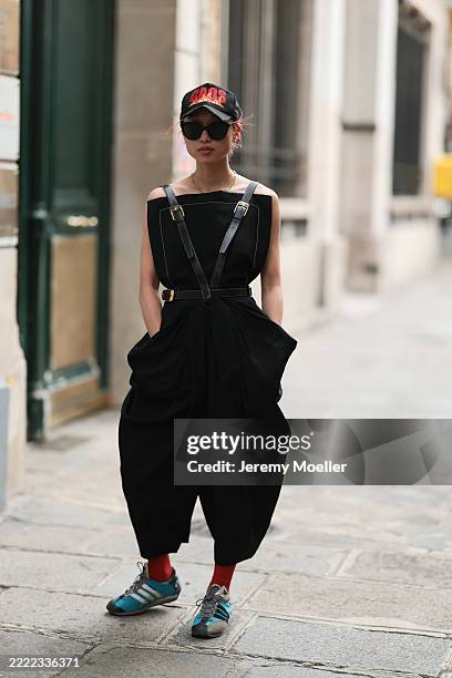 Fashion Week guest is seen wearing a black cap with red embroidery reading “CAOS” and a flame design; black butterfly sunglasses from Chanel; small...