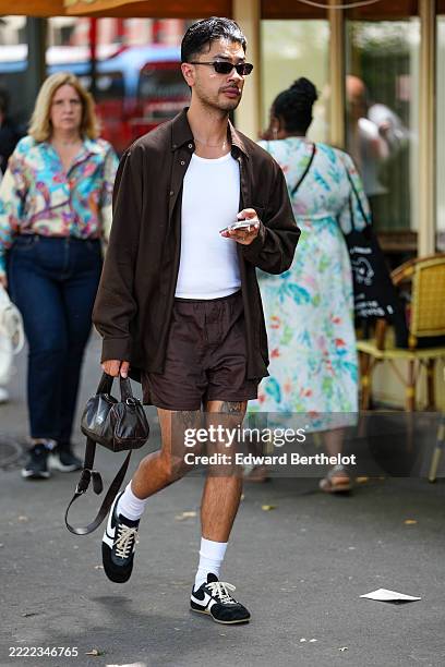 Guest wears a dark brown button-up shirt over a white tank top. The shirt is paired with matching dark brown shorts. Accessories include narrow, dark...