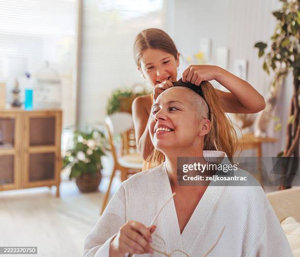 mère à la maison avec sa fille après la chimiothérapie et elle met sa perruque - cellule cancéreuse photos et images de collection
