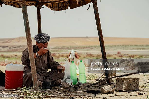 Kurdish man sits under a small makeshift canopy beside plastic bottles and a cooler near Lake Dukan in Ranya, Iraq, on June 30, 2025. The drought has...