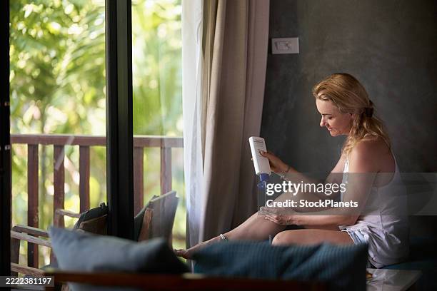 mujer sonriente aplicándose crema hidratante en la pierna en casa. - crema corporal fotografías e imágenes de stock