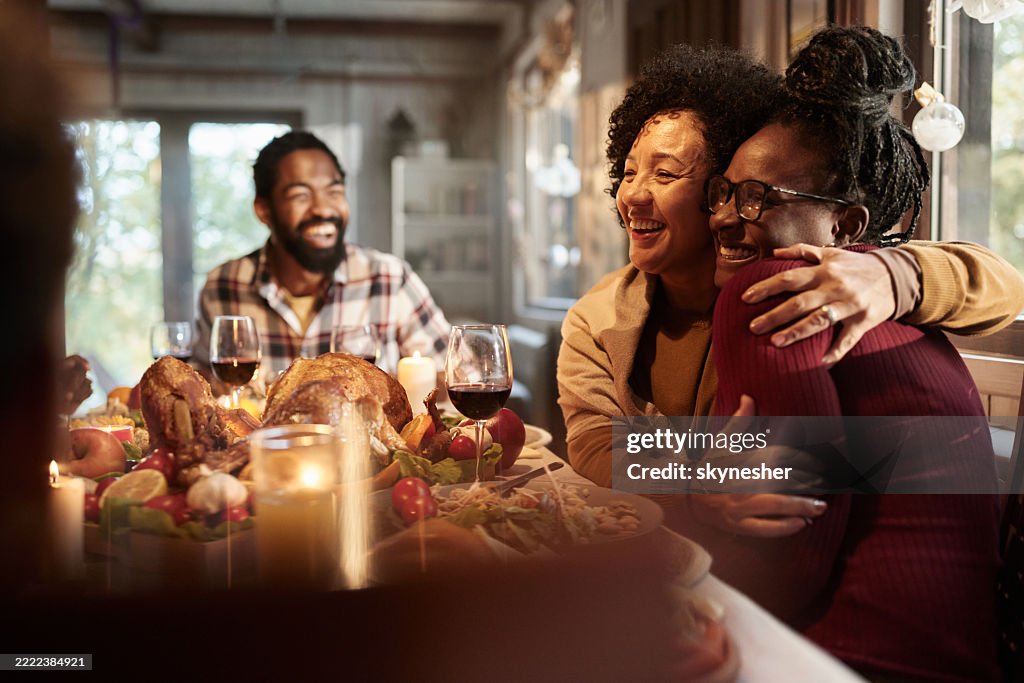 Happy black adult daughter and mother embracing during Thanksgiving lunch.