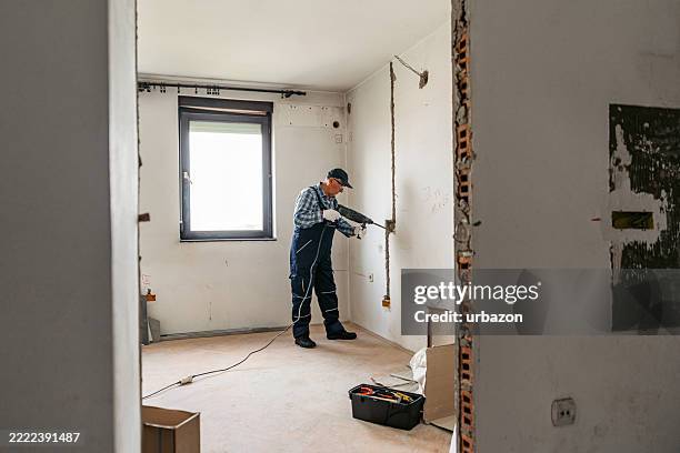 lavoratore maschio anziano che perfora il muro in un appartamento vuoto in ristrutturazione - trapano foto e immagini stock