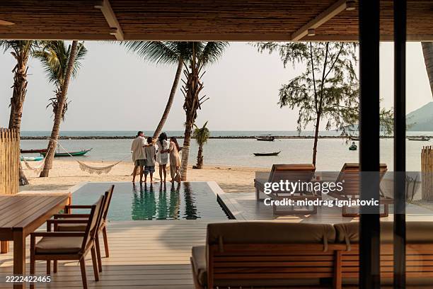 happy family embracing by the poolside of a villa overlooking the beach - hotel de luxo imagens e fotografias de stock