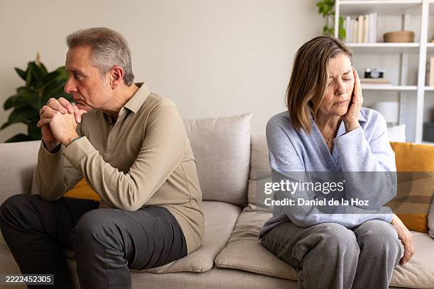senior couple having relationship problems sitting on sofa at home - husband stock pictures, royalty-free photos & images