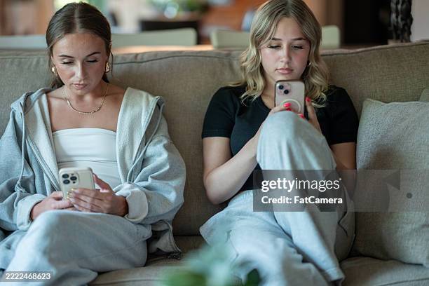 deux jeunes femmes occupées sur des smartphones assises sur un canapé à la maison - générique photos et images de collection