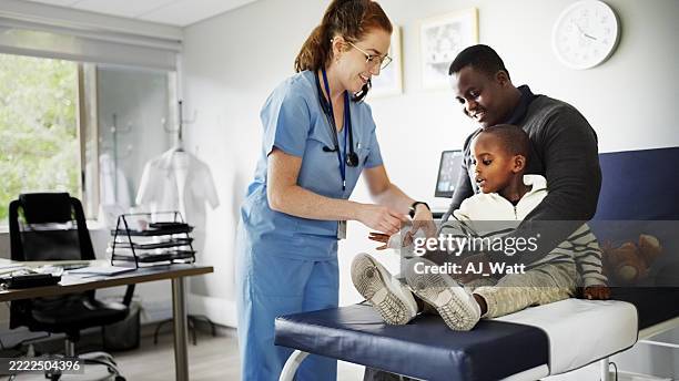 médico envolviendo gasa en la mano de un niño herido con el padre consolando en la clínica - esguince fotografías e imágenes de stock