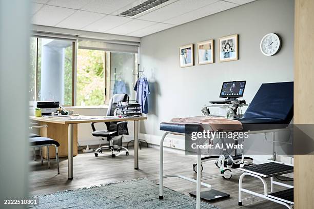 empty clinic room with desk and examination table - dokterspraktijk stockfoto's en -beelden