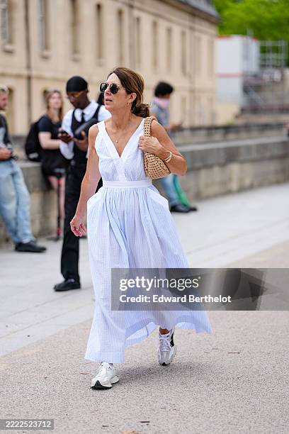 Guest wears aviator sunglasses and small hoop earrings. The hair is styled in a low ponytail. A sleeveless dress in light blue and white vertical...