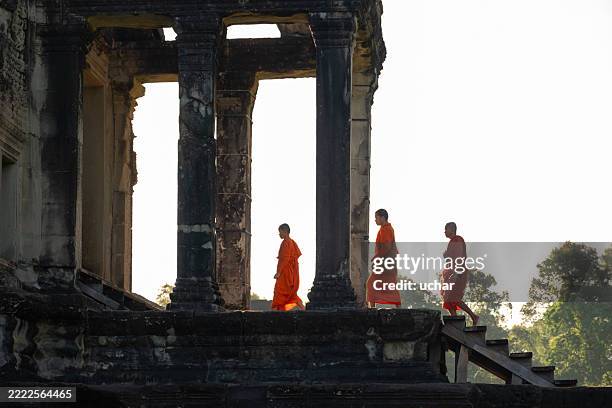 vier buddhistische mönche spazieren bei sonnenaufgang durch den alten angkor wat-tempel in siem reap, kambodscha - siemreap tempelkomplex stock-fotos und bilder