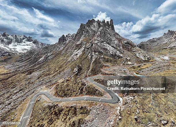 dramatic high-altitude mountain landscape with a winding serpentine road leading towards rugged. a partially frozen river adds to the wild, adventurous beauty at lianbaoyeze is a breathtaking high-altitude mountain range in sichuan, china - bergpass stock-fotos und bilder
