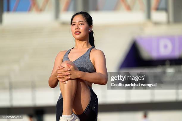 young asian woman stretching leg muscles on a track, preparing for a run while enjoying the warm sunlight during outdoor training - running shorts stock pictures, royalty-free photos & images