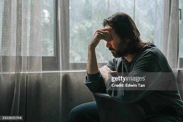 hombre melancólico sentado junto a la ventana en profundo pensamiento - fragilidad fotografías e imágenes de stock