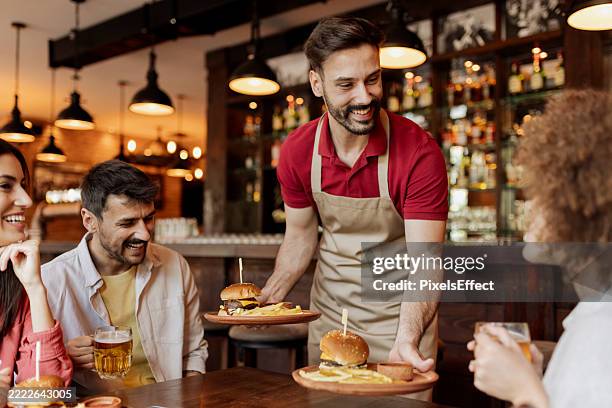 friendly waiter serving burgers to happy customers at pub - ober stockfoto's en -beelden