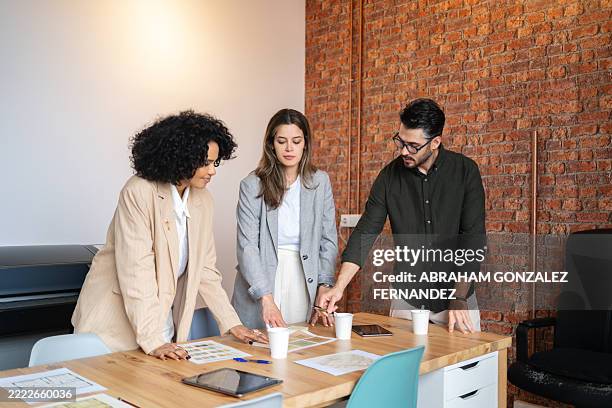 tre architetti stanno esaminando i progetti e discutendo i piani di progetto in un moderno ambiente d'ufficio - designer industriale foto e immagini stock
