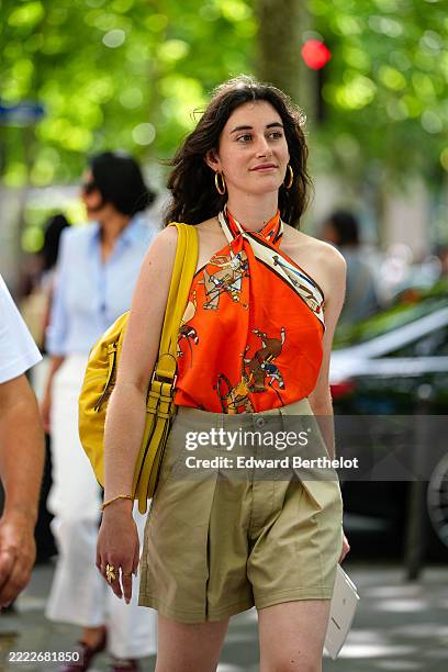 Guest wears gold hoop earrings, bright orange horse graphic pattern/print Hermes scarf top, dark yellow leather bag, light brown high waisted khaki...