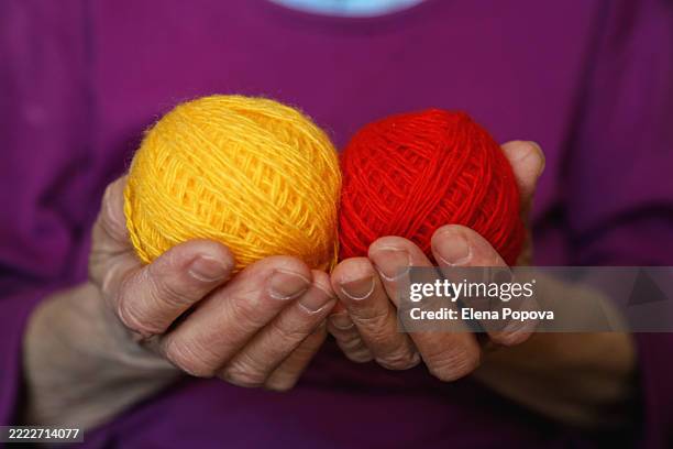 cropped hands elderly woman holding vibrant red and yellow balls of wool - gomitolo di lana foto e immagini stock