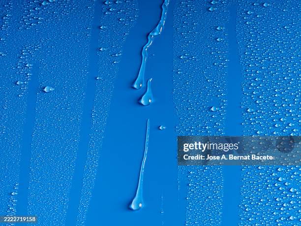 wet surface with raindrops sliding on a blue background. - regentropfen stock-fotos und bilder
