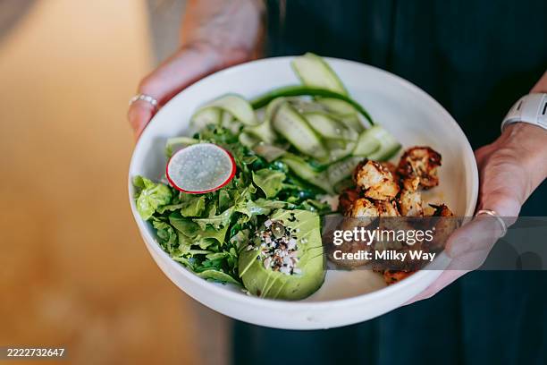 woman holding white bowl with green salad, avocado, grilled shrimps, cucumber ribbons, radish slice. casual dining. - ketogenic diet stock pictures, royalty-free photos & images
