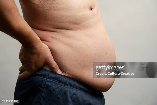 profile view of man with pot belly against gray background - abdomen humano fotografías e imágenes de stock