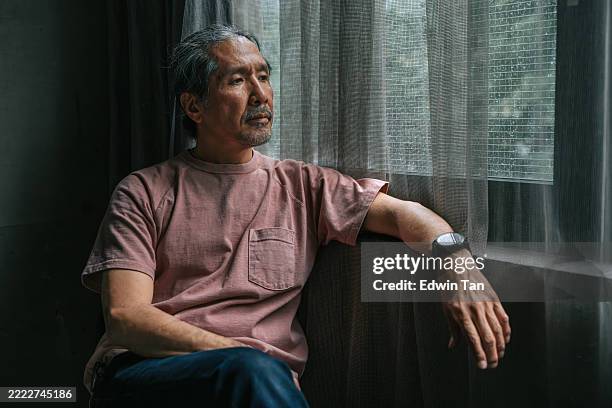pensive mature japanese man sitting by rainy window - hopelessness stock pictures, royalty-free photos & images