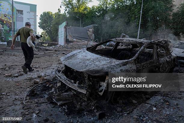 Man carrying a dog walks past the wreckage of cars following mass Russian drones and missile strike on the Ukraine's capital Kyiv on July 4 amid the...