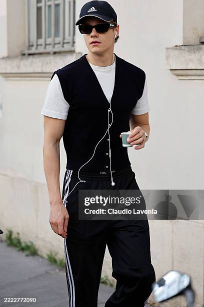 Florian Macek wears white t-shirt, black vest, black Adidas sweatshirt, black Adidas cap, outside White Mountaineering, during the Menswear...
